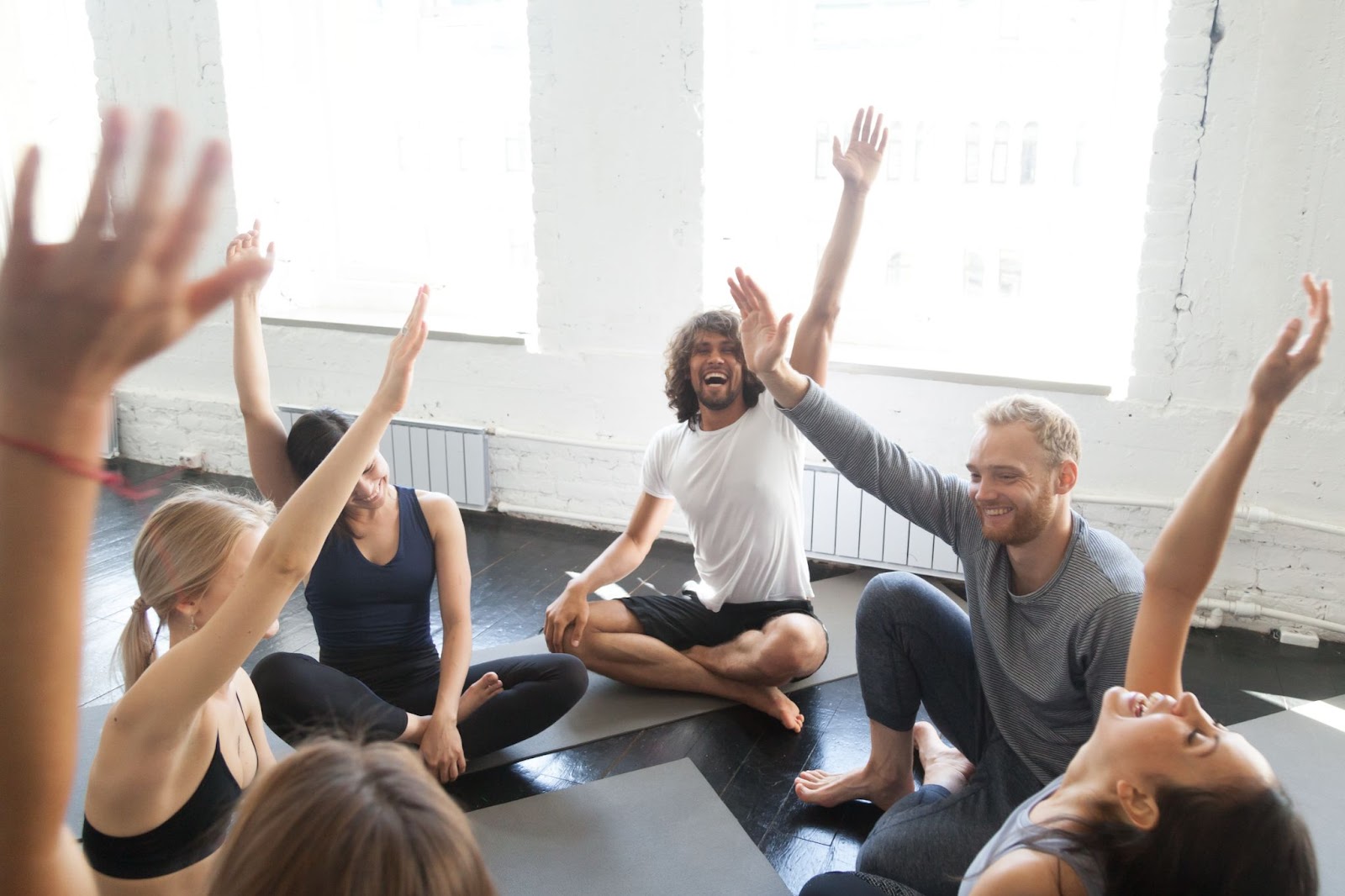 A group of men and women laughing with their hands up during a yoga class.