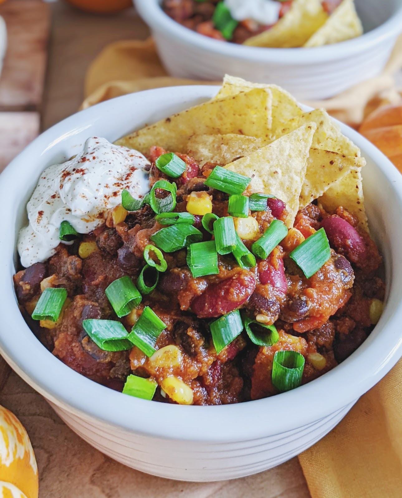 close up of a bowl of pumpkin chili topped with green onions and tortilla chips