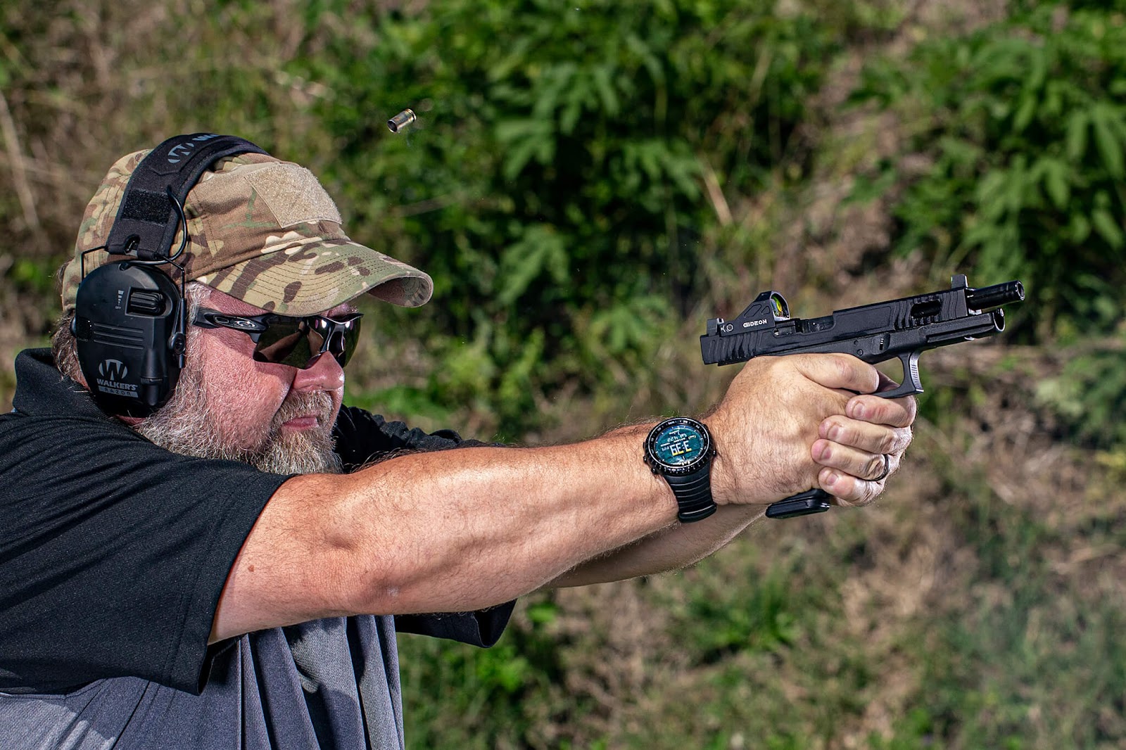 Side angle of a man shooting a firearm with an optic attached