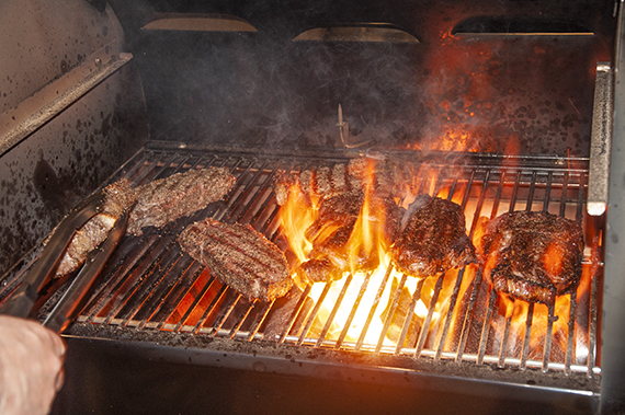 Several steaks grilling over a hot grill with flames.