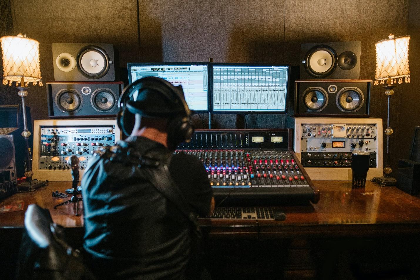 A man sitting facing a sound mixer with his headphones on in a recording studio-How To Produce Music For Beginners- Essential Tips