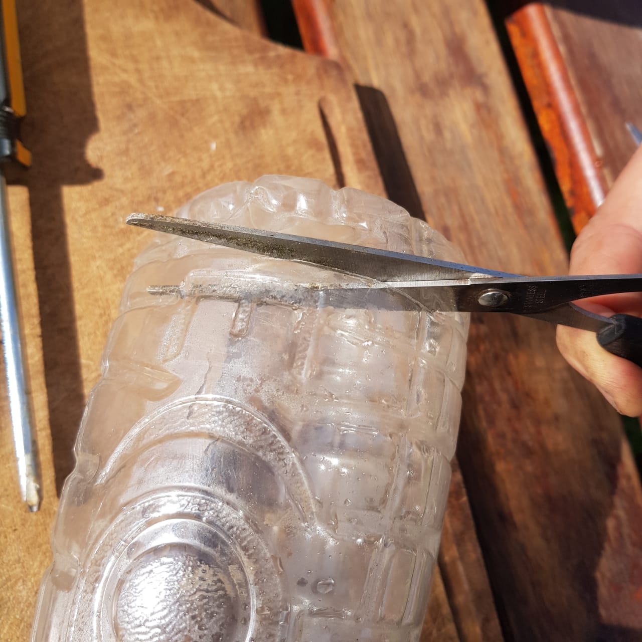 una mano utilizando una tijera para recortar la base de una botella de plástico.