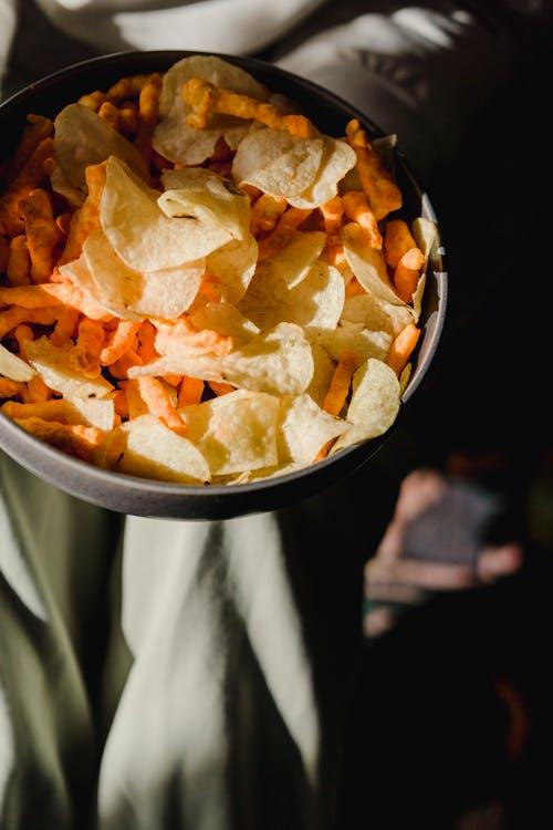From above of ceramic bowl with delicious chips and snacks against textured surface