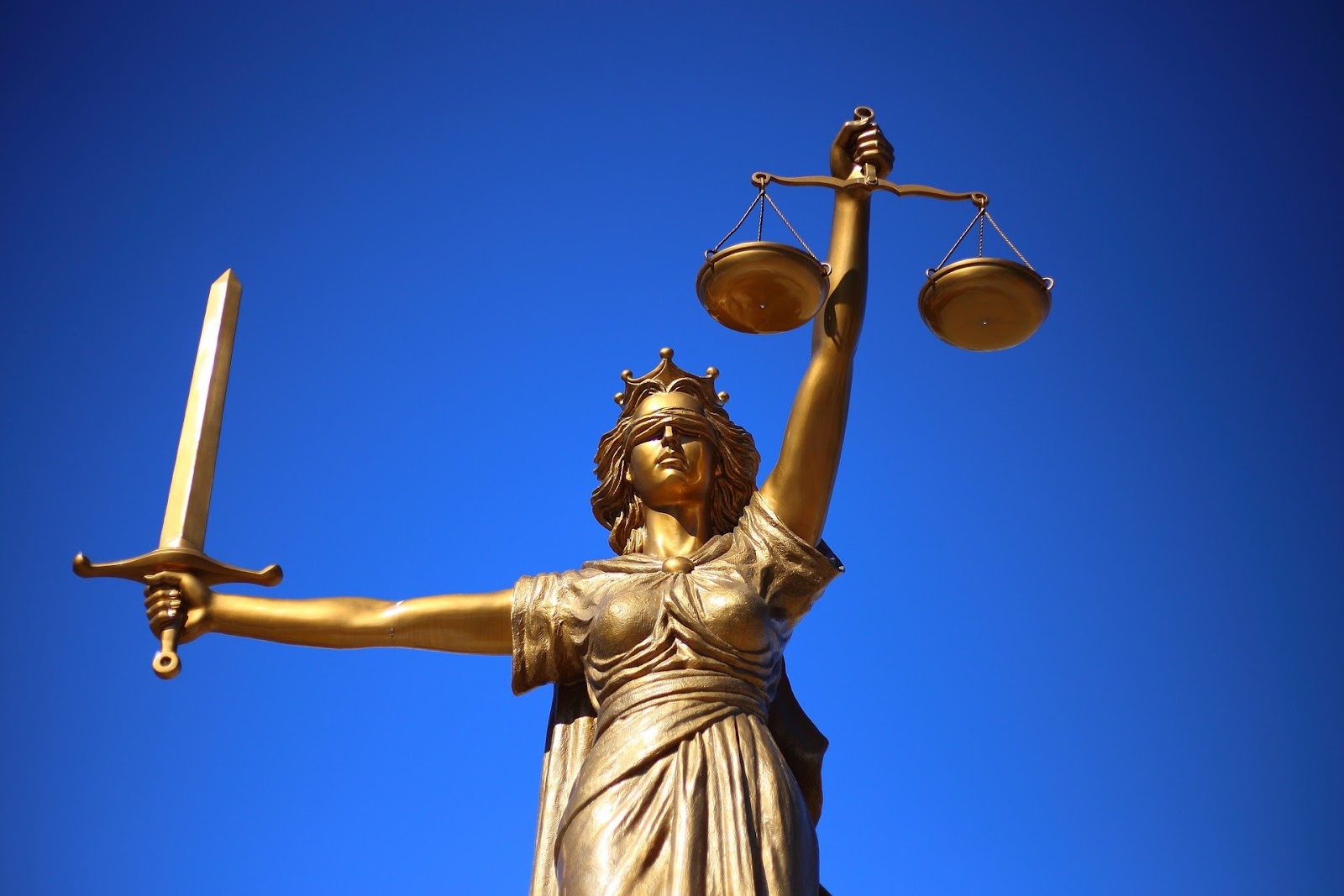 A picture of a gold statue lady justice, blindfolded, holding the scales of justice in one hand and a sword in the other