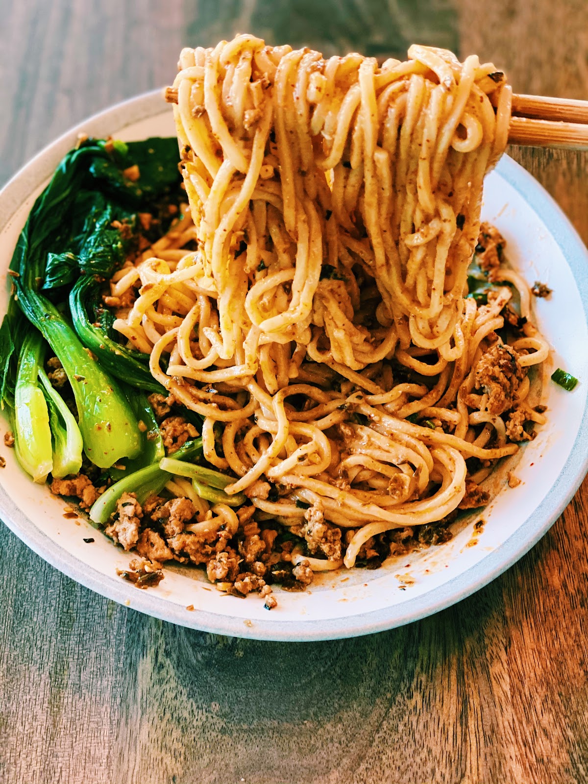 A bowl of Dan Dan Noodles, egg noodles mixed with spicy chili ground pork and garnished with baby bok choy and green onions
