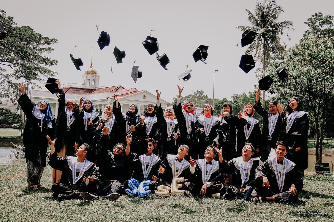 People in Blue Academic Dress Sitting on Green Grass Field