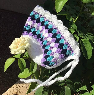 white, lavender, teal and black baby bonnet with flowers and leaves in background