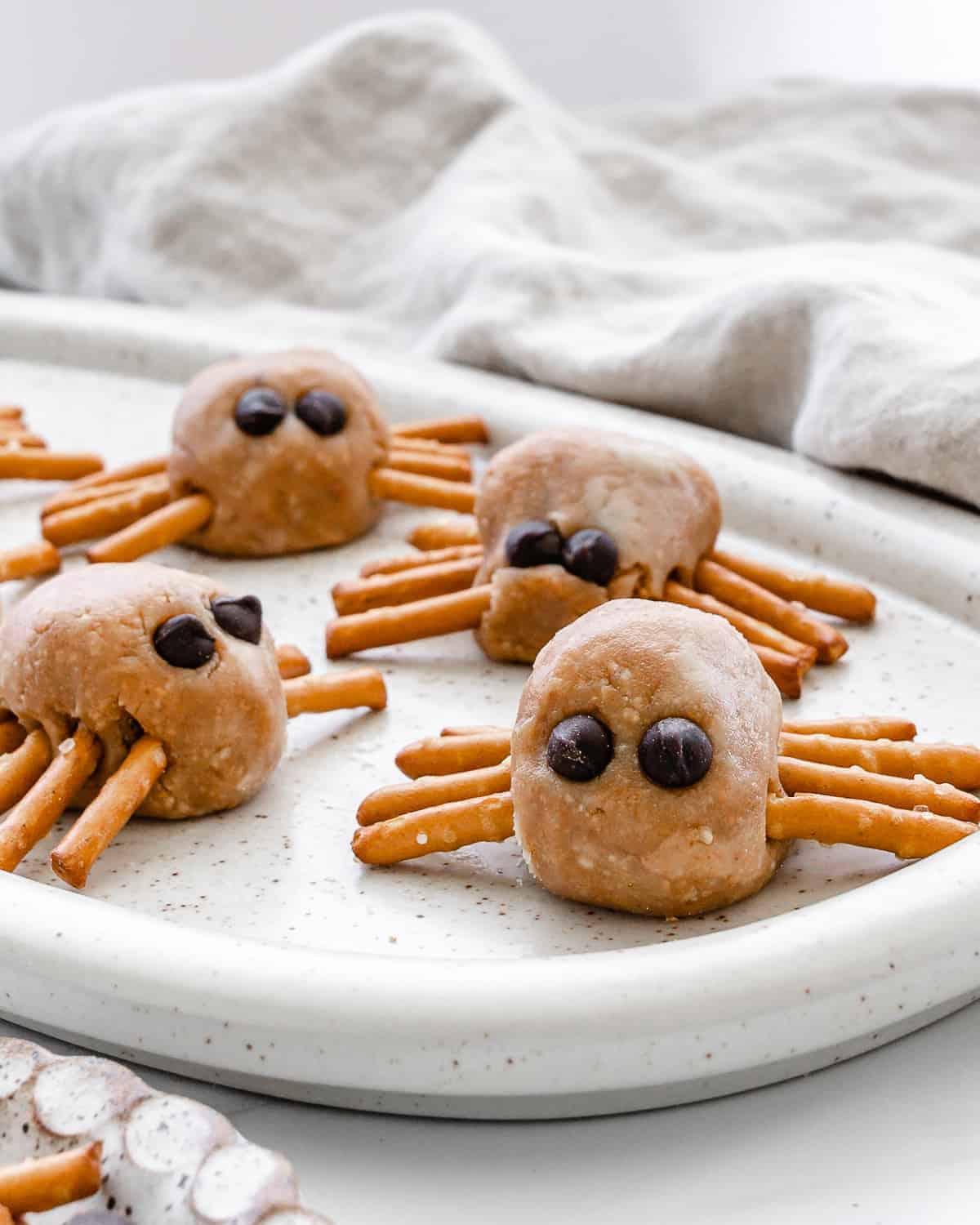 Peanut butter no bake protein balls, decorated as spiders, displayed on a white plate for Halloween.