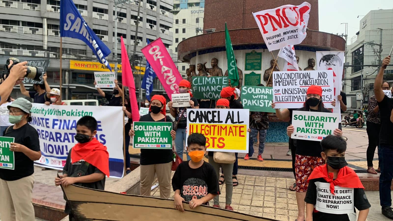 A dozen protesters with signs stand in a public square in Manilla