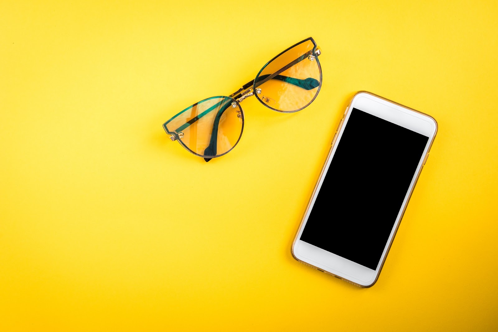 Mobile phone and eye glasses on a yellow background