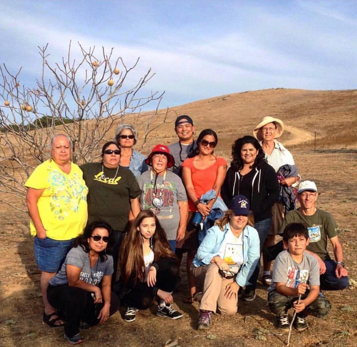 Attendees of the California Indian Conference hike on Bay Miwok land with Indigenous elders and youth and a young California Buckeye tree in the background.