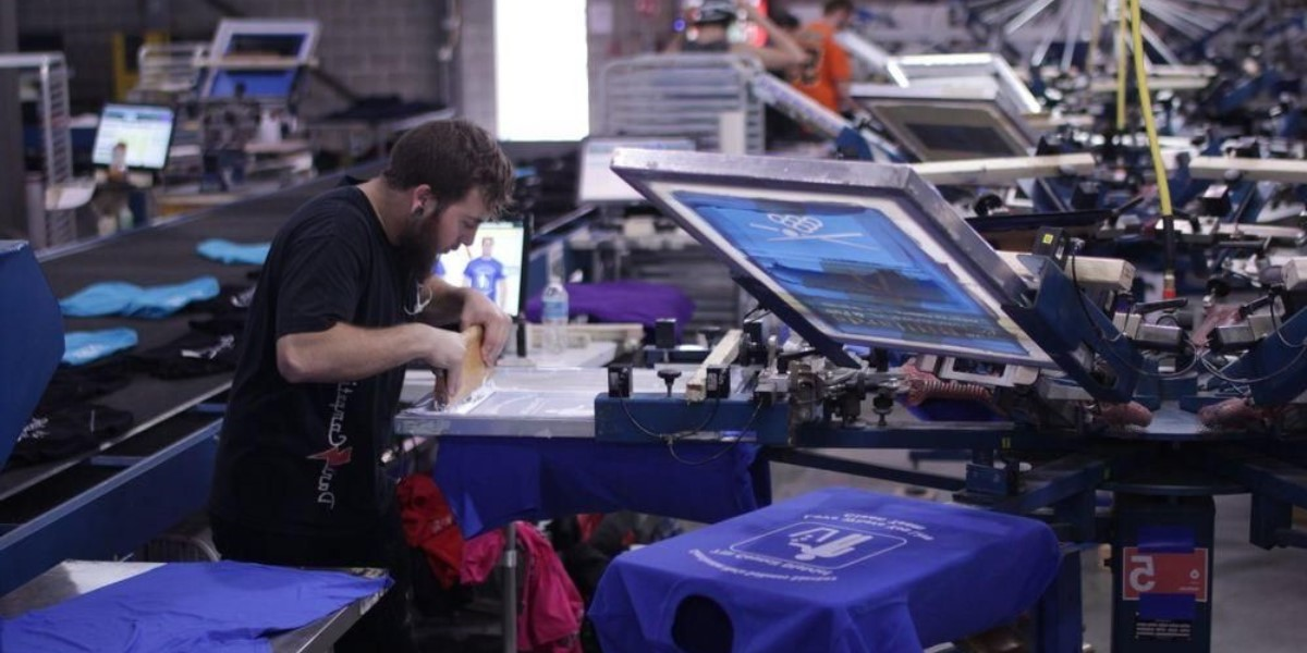 a man printing blue t-shirts with a DTG printer