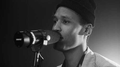 Free Grayscale Photo of a Man with a Beanie Singing on a Microphone Stock Photo