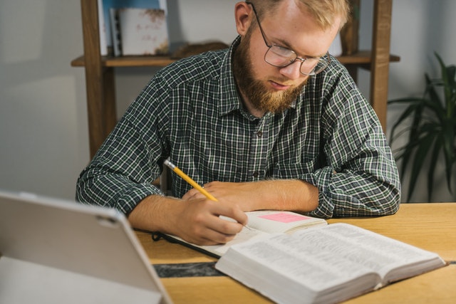 Man in his home library busy studying the word of God and taking notes on his desk