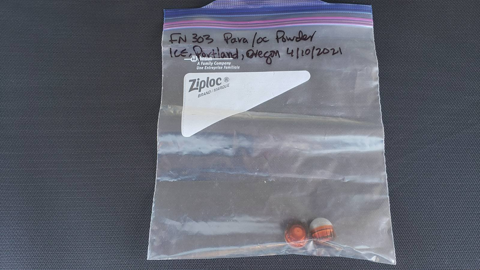 A ziploc baggie with two unexploded FN 303 PAVA/OC rounds inside. They are a dark orange color with a clear top. 

Writing, in sharpie, on the baggie identifies the munitions and says "ICE, Portland, Oregon 4/10/2021."