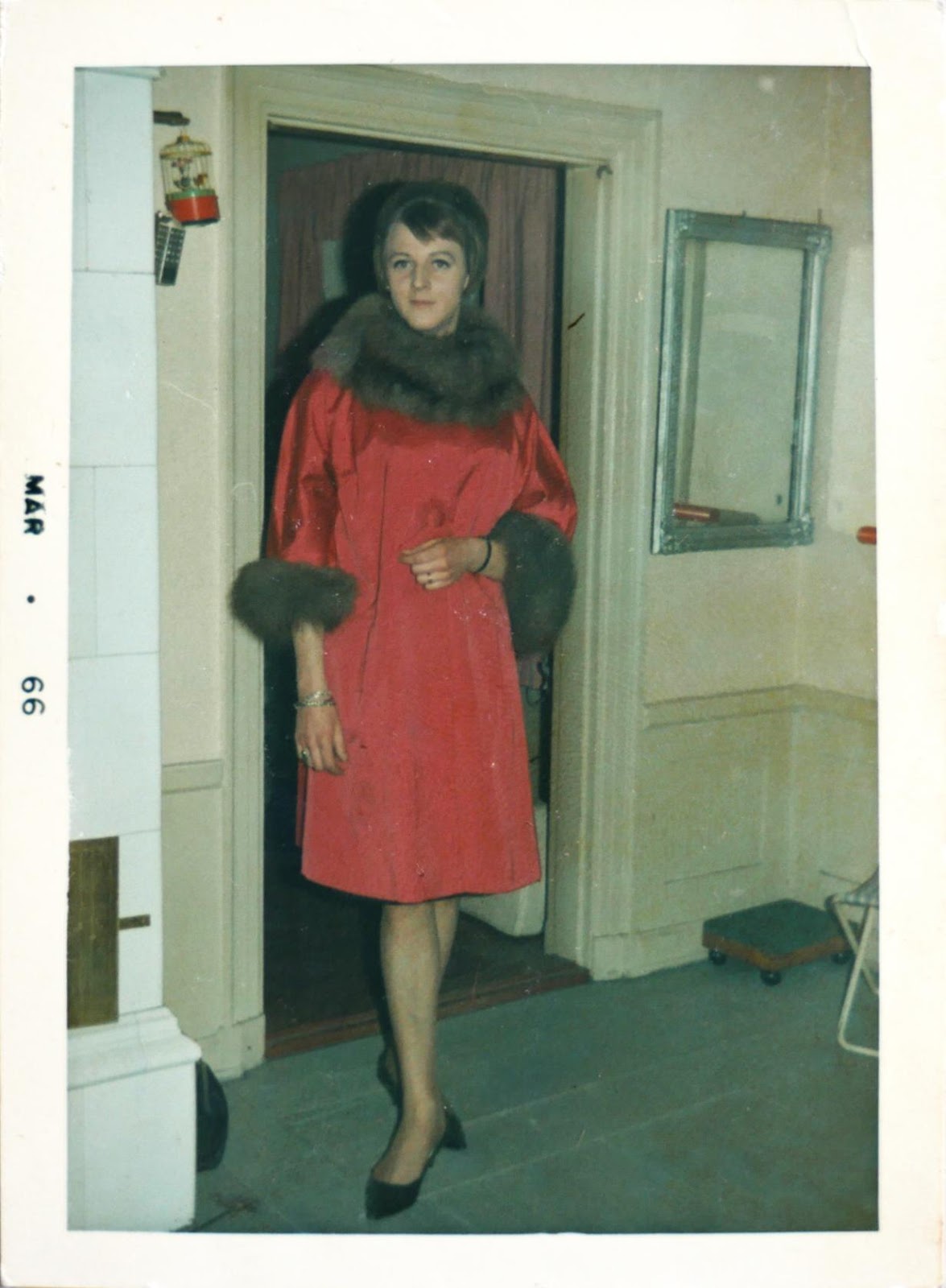 en kvinna i  fin röd sidenkappa med pälsdetaljer. fotot ser gammalt ut. I ramen står mar 66.