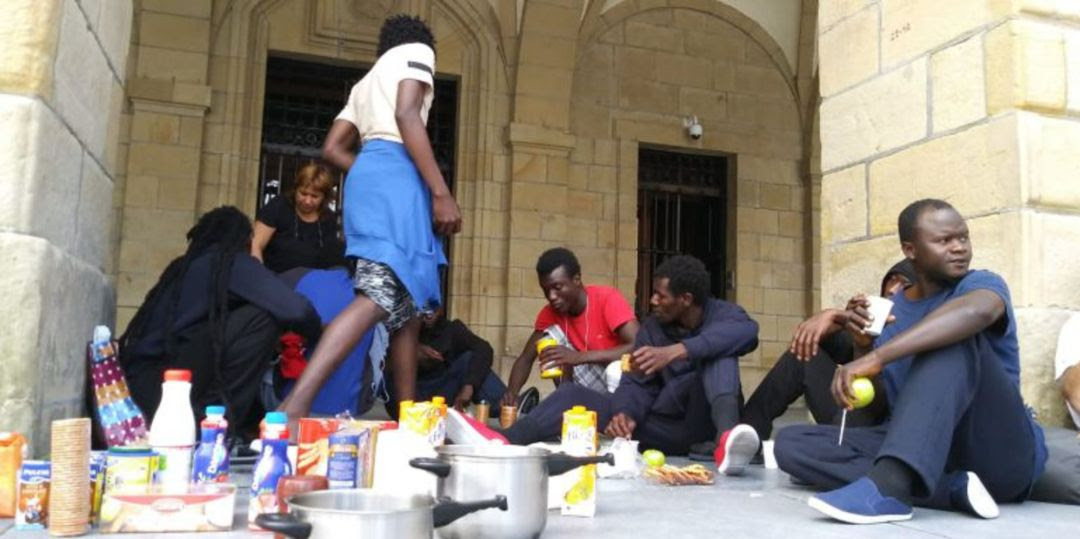 Persona migrantes recibiendo alimentos de la Red de Acogida Ciudadana en los arkupes del Ayuntamiento de Irun.