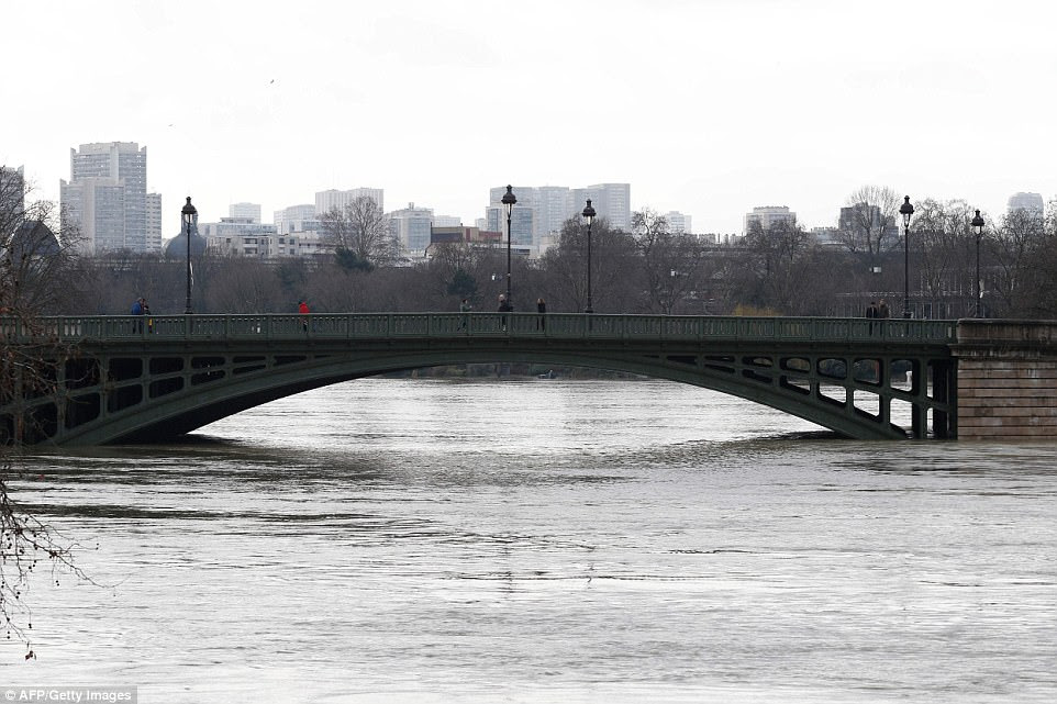 People cross a bridge over the swollen Seine river in Paris today. A main commuter line, the RER C, has halted service at Paris stops until Wednesday, and some expressways that run alongside the Seine have been closed
