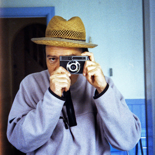 reflected self-portrait with Agfa Isomat-Rapid camera and back to front straw hat by pho-Tony