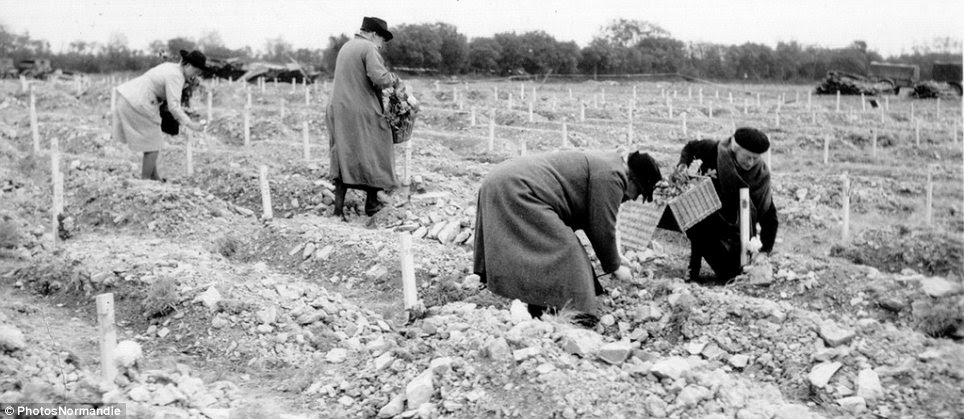 Helping hand: Four civilians carry baskets full of flowers around a temporary cemetery, placing one on each grave