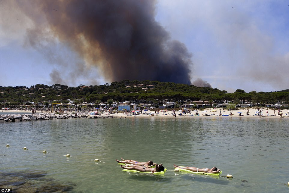 Three topless women on inflatable lilos try not to let the fire ruin their day at the beach as they soak in the sun in Lavandou, French Riviera