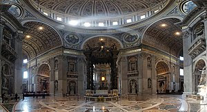 Foto amplo ângulo de interior. Detalhes visíveis nesta vista incluem: uma faixa dourada de texto que se estende ao redor da cornija, nichos com estátuas em todos os cais, anjos esculpidos ao redor do arcos, e no chão de mármore incrustado, a concepção de que irradia a partir do baldaquino sob a cúpula.