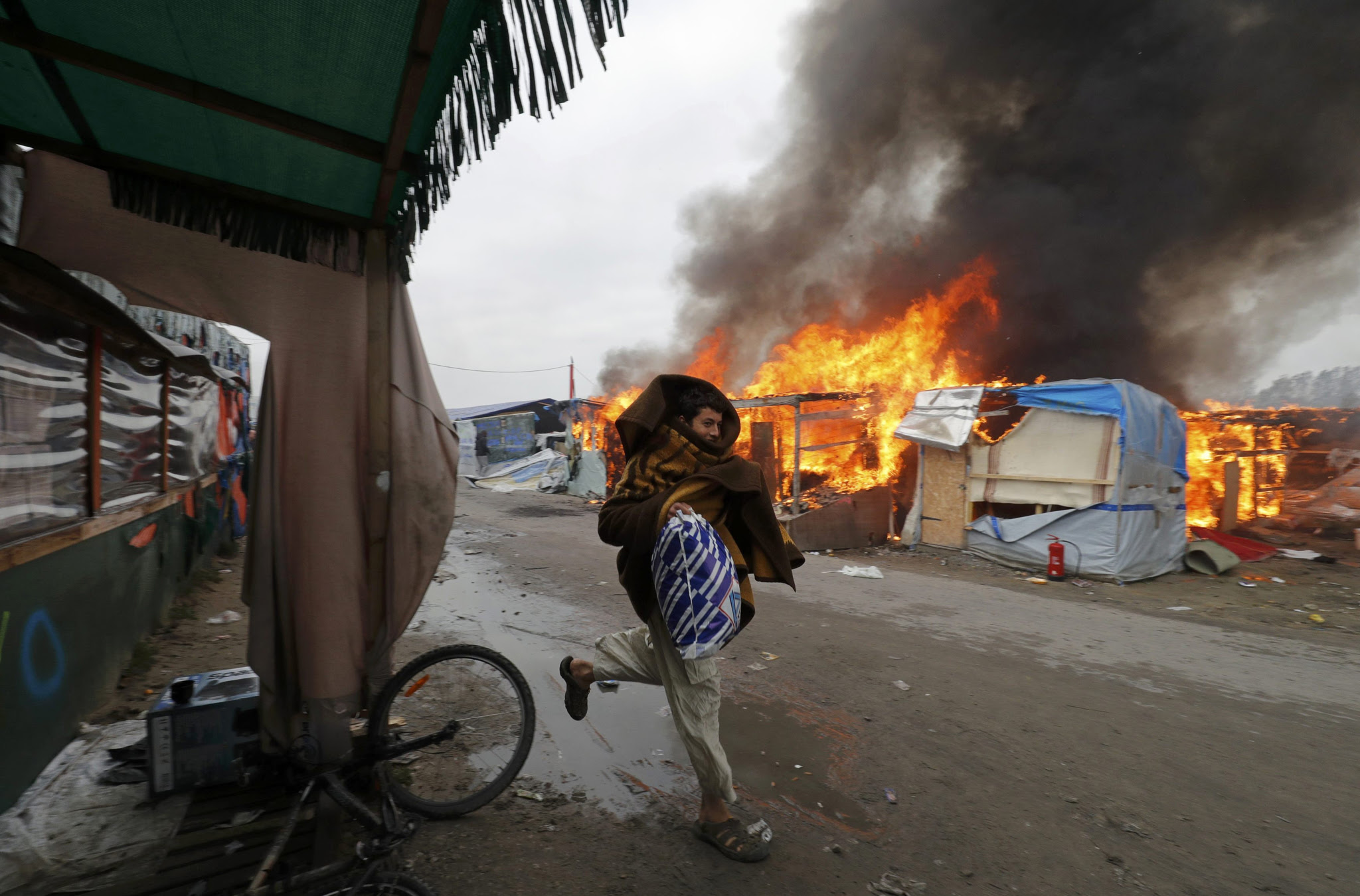 A migrant runs past a burning makeshift shelters in the "Jungle" on the third day of their evacuation and transfer to reception centers in France, as part of the dismantlement of the camp in Calais, France