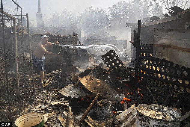 Dressed in a pair of swimming trunks, this man throws water on the remains of his burning possessions