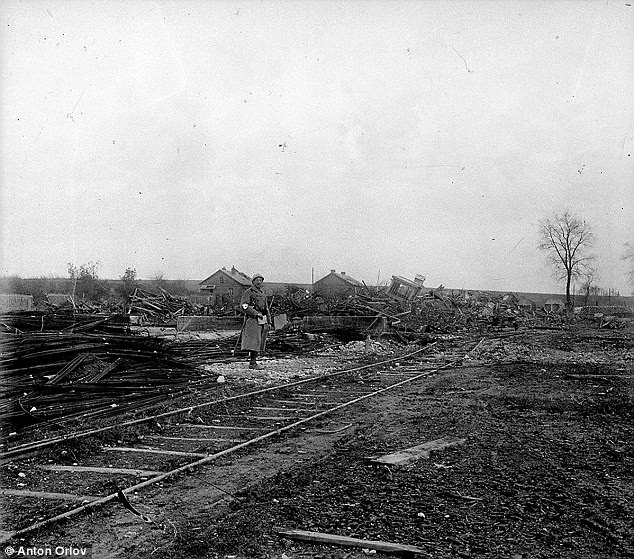 Ruins: A man in a long coat stands beside stacked lumber and destroyed homes, as well as an uprooted railroad track
