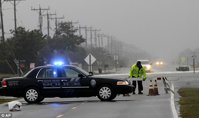 A police officer sets up a road block on South Oregon Inlet Road as water from Hurricane Sandy covers the road in Nags Head, North Carolina this morning 