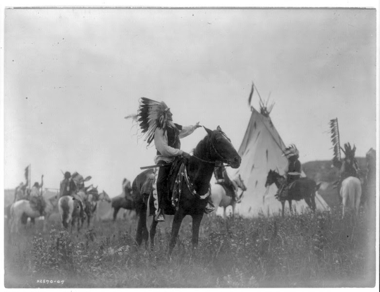 Description of  Title: Village herald.  <br />Date Created/Published: c1907 December 26.  <br />Summary: Dakota man, wearing war bonnet, sitting on horseback, his left hand outstreched toward tipi in background, others on horseback.  <br />Photograph by Edward S. Curtis, Curtis (Edward S.) Collection, Library of Congress Prints and Photographs Division Washington, D.C.