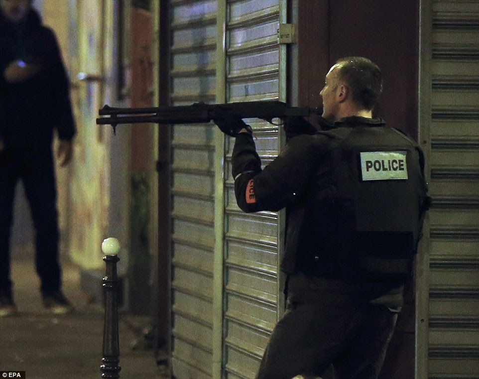 A French police officer takes cover while on the lookout for the shooters who attacked the restaurant 'Le Petit Cambodge'
