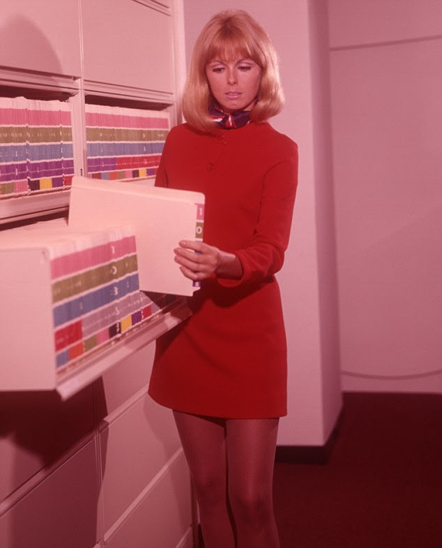 The thigh's the limit! A blonde-haired woman stands by a filing cabinet in a scarlet mini dress