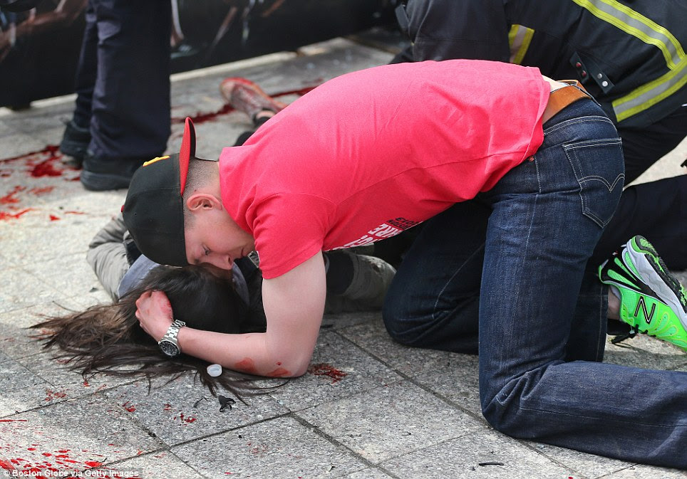 A man comforts an injured woman on the sidewalk at the scene of the first explosion on Boylston Street near the finish line of the Boston Marathon
