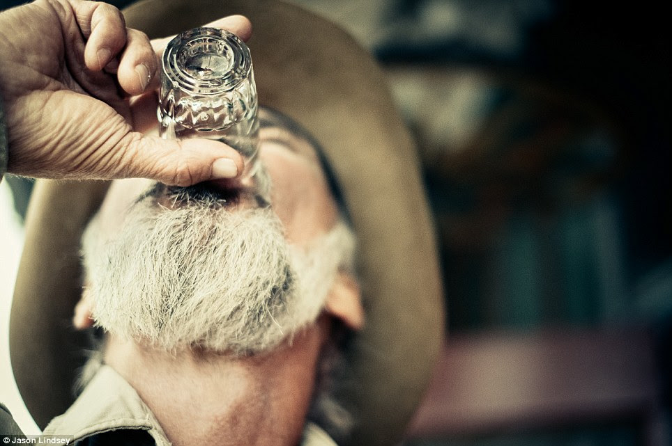 A rancher drinks from a shot glass as he takes a rest from a long day on the farm