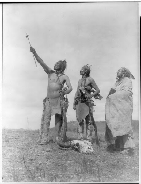 Description of  Title: The Oath--Apsaroke.  <br />Date Created/Published: c1908 November 19.  <br />Summary: Three Apsaroke men gazing skyward, two holding rifles, one with object skewered on arrow pointed skyward, bison skull at their feet.  <br />Photograph by Edward S. Curtis, Curtis (Edward S.) Collection, Library of Congress Prints and Photographs Division Washington, D.C.