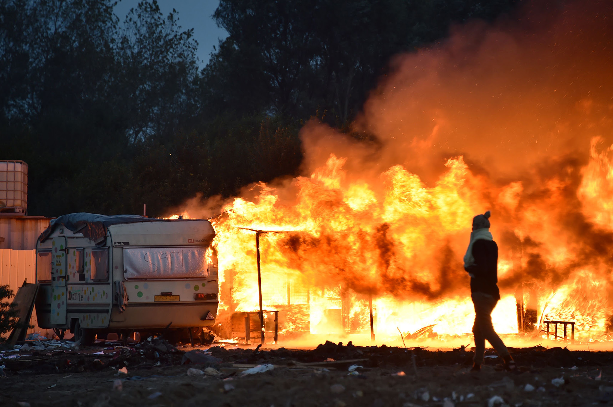 A woman walks past a burning structure at the "Jungle" migrant camp in Calais, northern France, early on October 28, 2016, after a massive operation to clear the settlement where 6,000-8,000 people have been living. Migrants left behind after the demolition of France's notorious "Jungle" faced a day of reckoning on October 28 after spending the night, with official blessing, in a disused part of the camp. / AFP PHOTO / PHILIPPE HUGUENPHILIPPE HUGUEN/AFP/Getty Images
