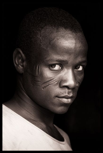 Africa | "An intense encounter at Nadoba". Young Tamberma man from Togo with heavy facial scars and an intense look.  | ©John Kenny