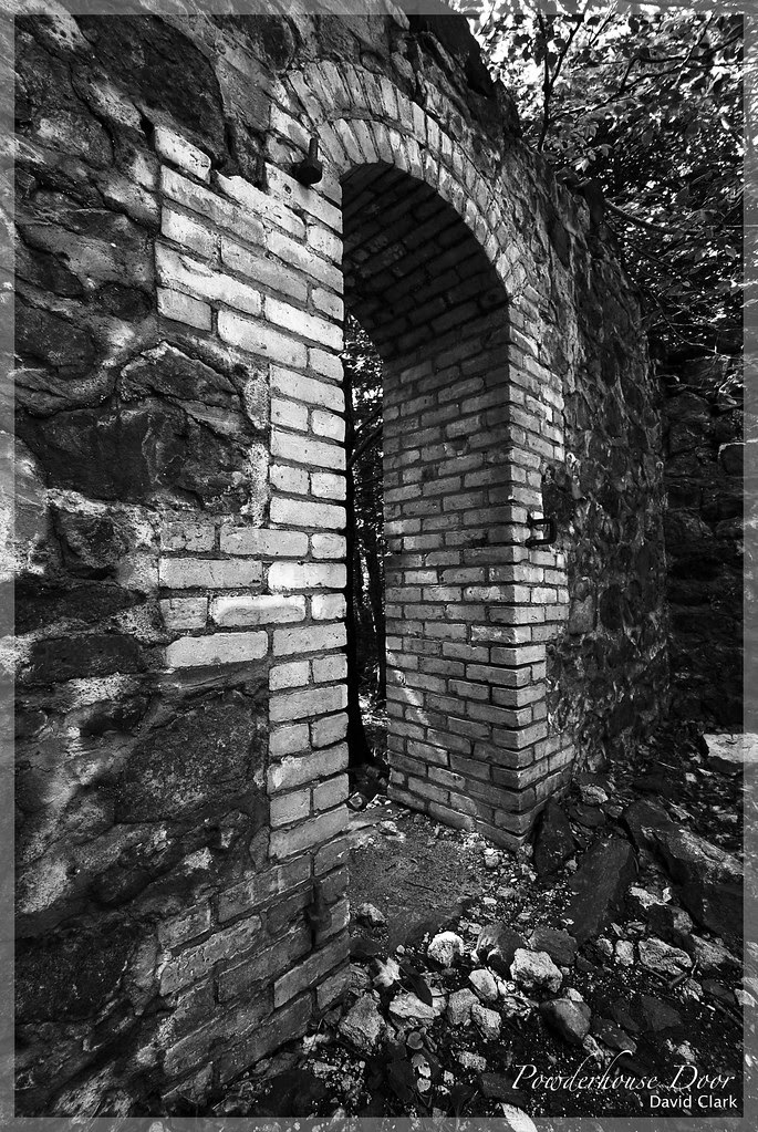 A wide angle shot of a brick  doorway in the middle of poor rock walls, all ruined.