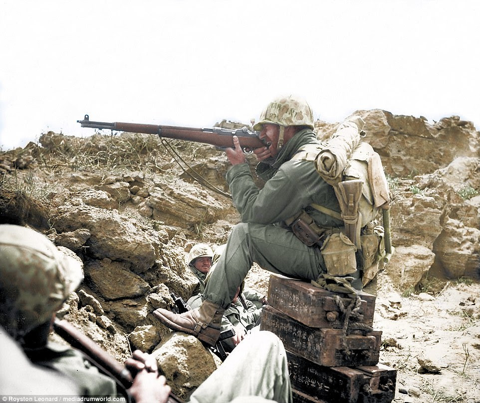 Pictured, a US marine sitting on Japanese ammunition boxes takes aim using his M1 Garand at Iwo Jima in 1945