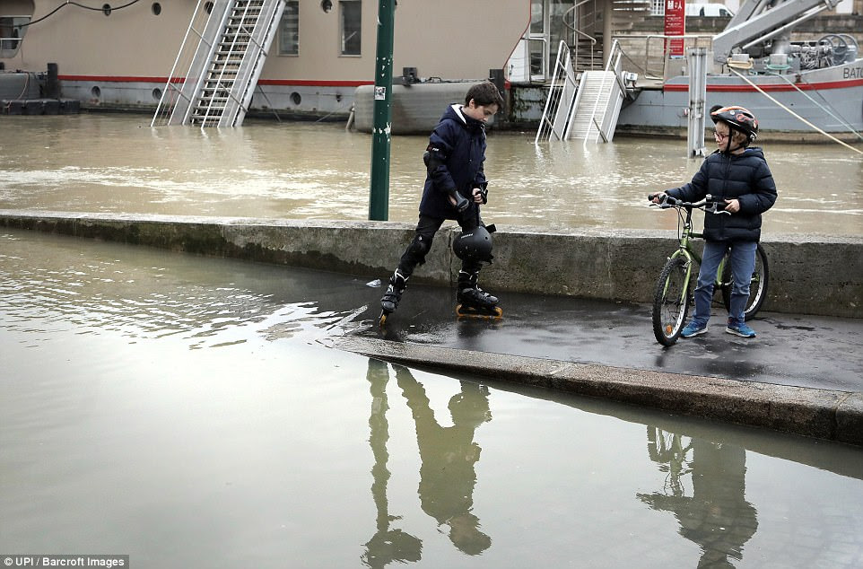 In the south of France, heavy rains caused a breach in the water supply pipe of a holding tank on an oil platform in La Mede, near Marseille, on Saturday, French giant Total said. Pictured: Children playing in the swollen river 