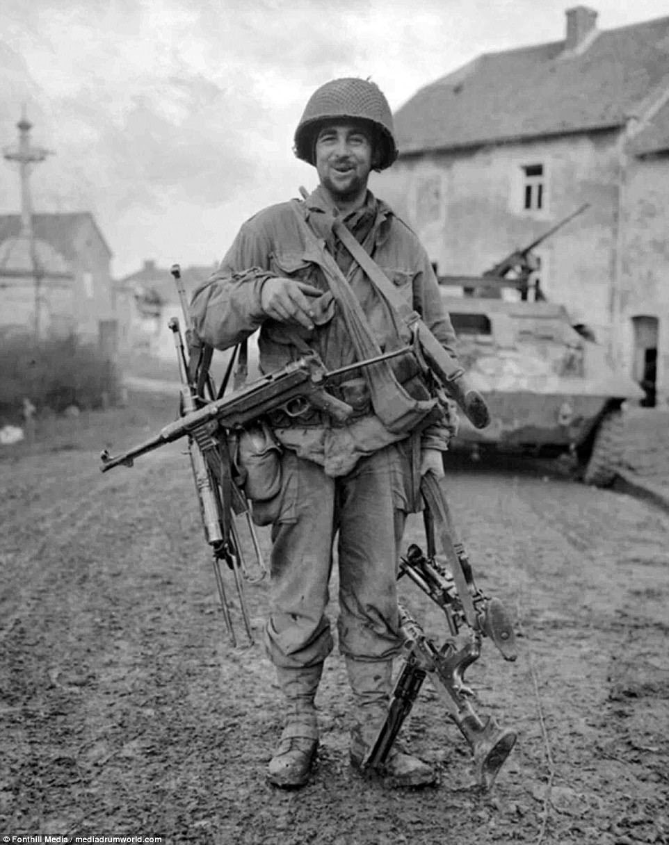 An American soldier grins as he holds up captured weapons during the offensive over the winter 1944/1945