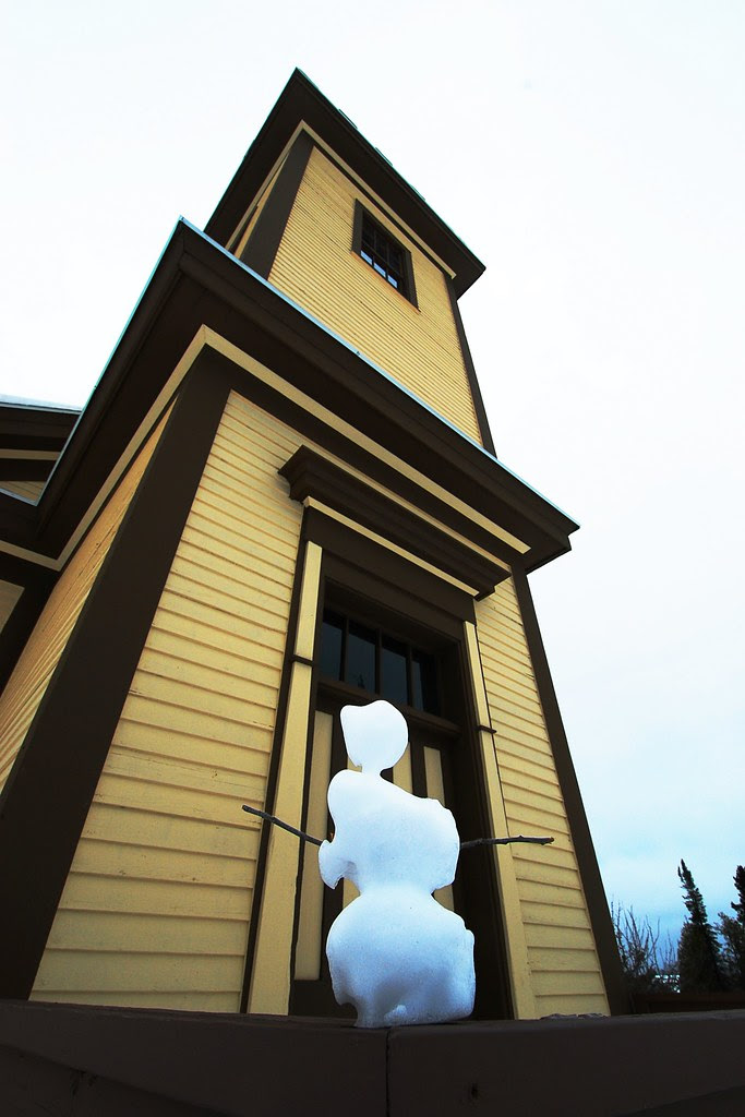 A snowman built in front of a small church.