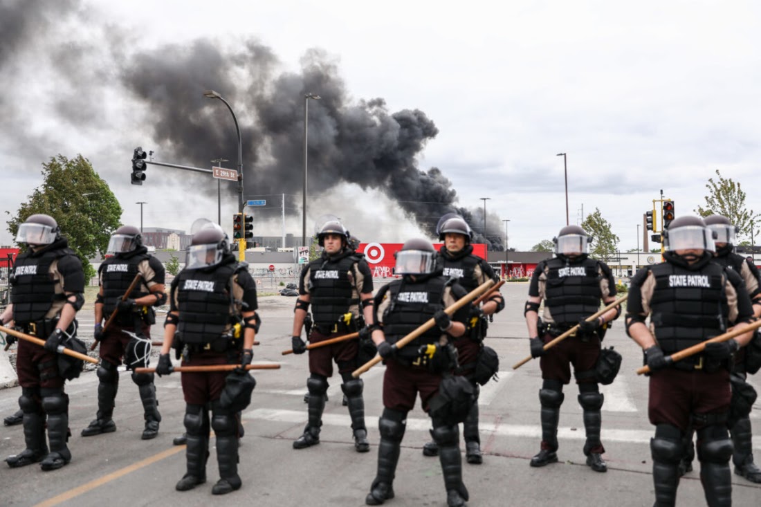 Cảnh sát tiểu bang đứng ra bảo vệ khi những làn khói từ các tòa nhà tiếp tục bốc cháy sau một đêm biểu tình và bạo lực sau cái chết của George Floyd, tại thành phố Minneapolis, bang Pennsylvania, vào ngày 29/5/2020. (Charlotte Cuthbertson / The Epoch Times)
