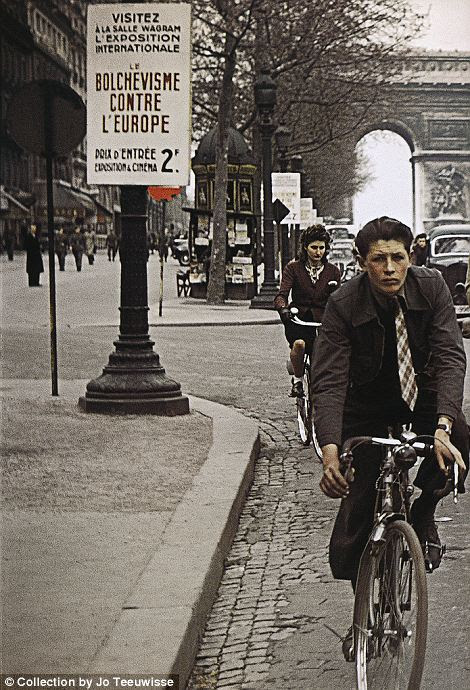 Grim-faced Parisian commuters cycle past another poster for the Europe Against Bolshevism exhibition
