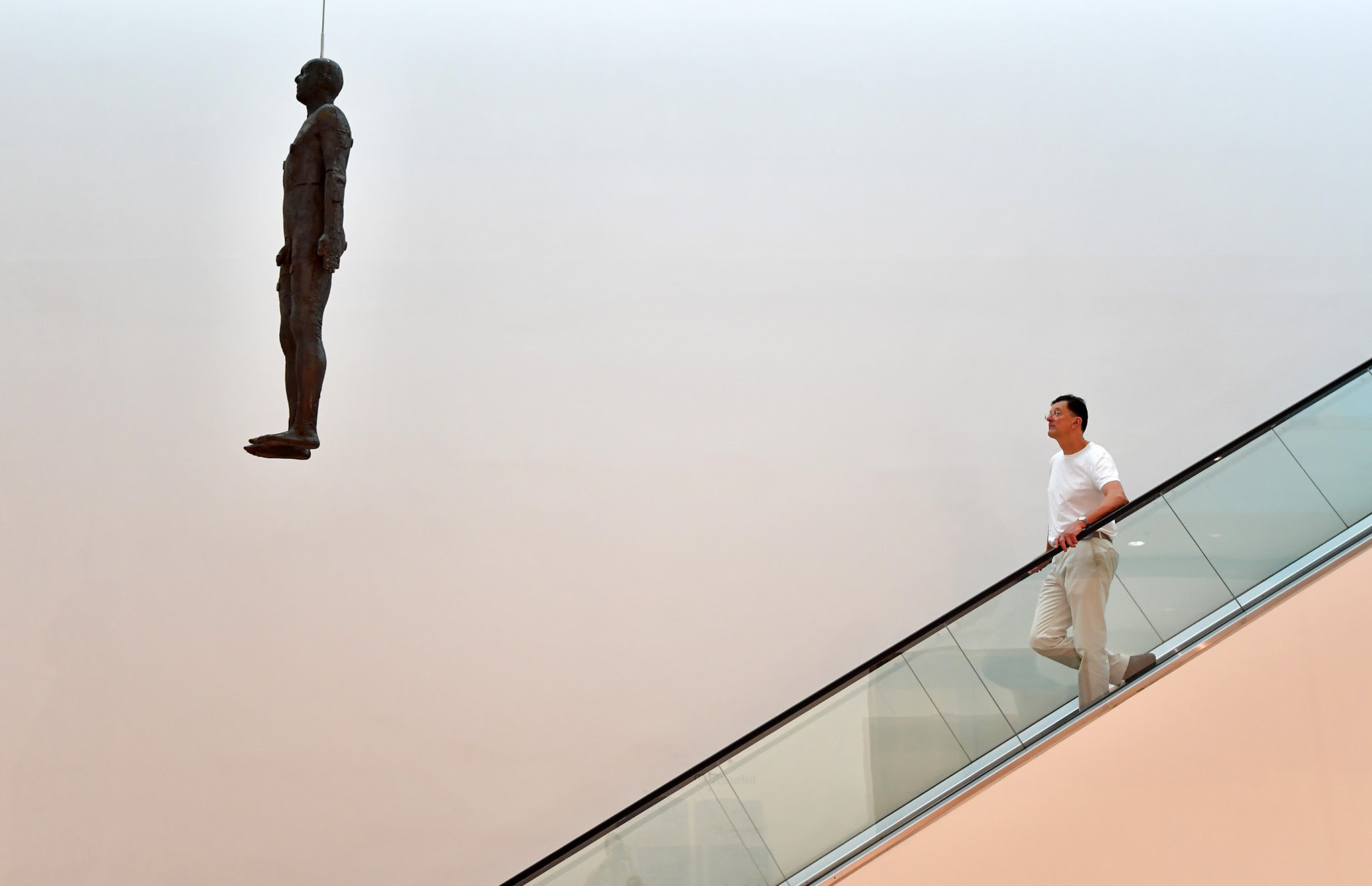 British artist Anthony Gormley poses for a photograph next to his artwork entitled 'Object, 199', a life-size cast-iron sculpture cast from the artist's body and hung from the ceiling of the National Portrait Gallery, during a press preview on September 7, 2016 in London, England. The work is accompanied on October 5 by 'Fall, 1999', a selection of drawings also by Mr Gormley.  (Photo by Carl Court/Getty Images)