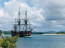 A three-masted sailing ship crossing a bay