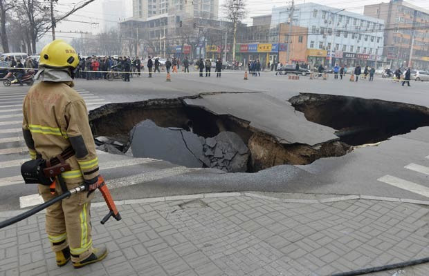 Policial guarda o buraco misterioso nesta quarta-feira (26) na cidade chinesa de  (Foto: Reuters)