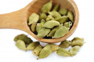 Cardamom seeds in the wooden spoon on white background