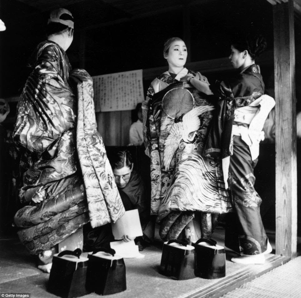 Japanese geisha girls, without their wigs, prepare themselves for the evening, having their kimonos pinned on and getting ready to slip into their platform flip-flops